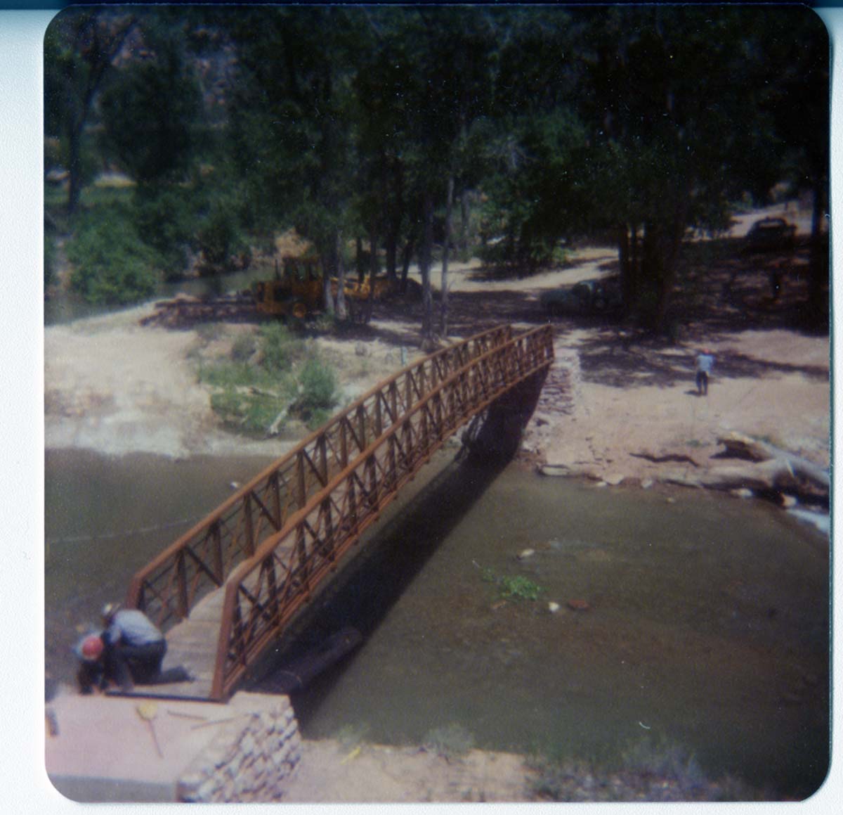 Two men working on the new Grotto footbridge across the Virgin River, equipment in background. Before trail created to access bridge.