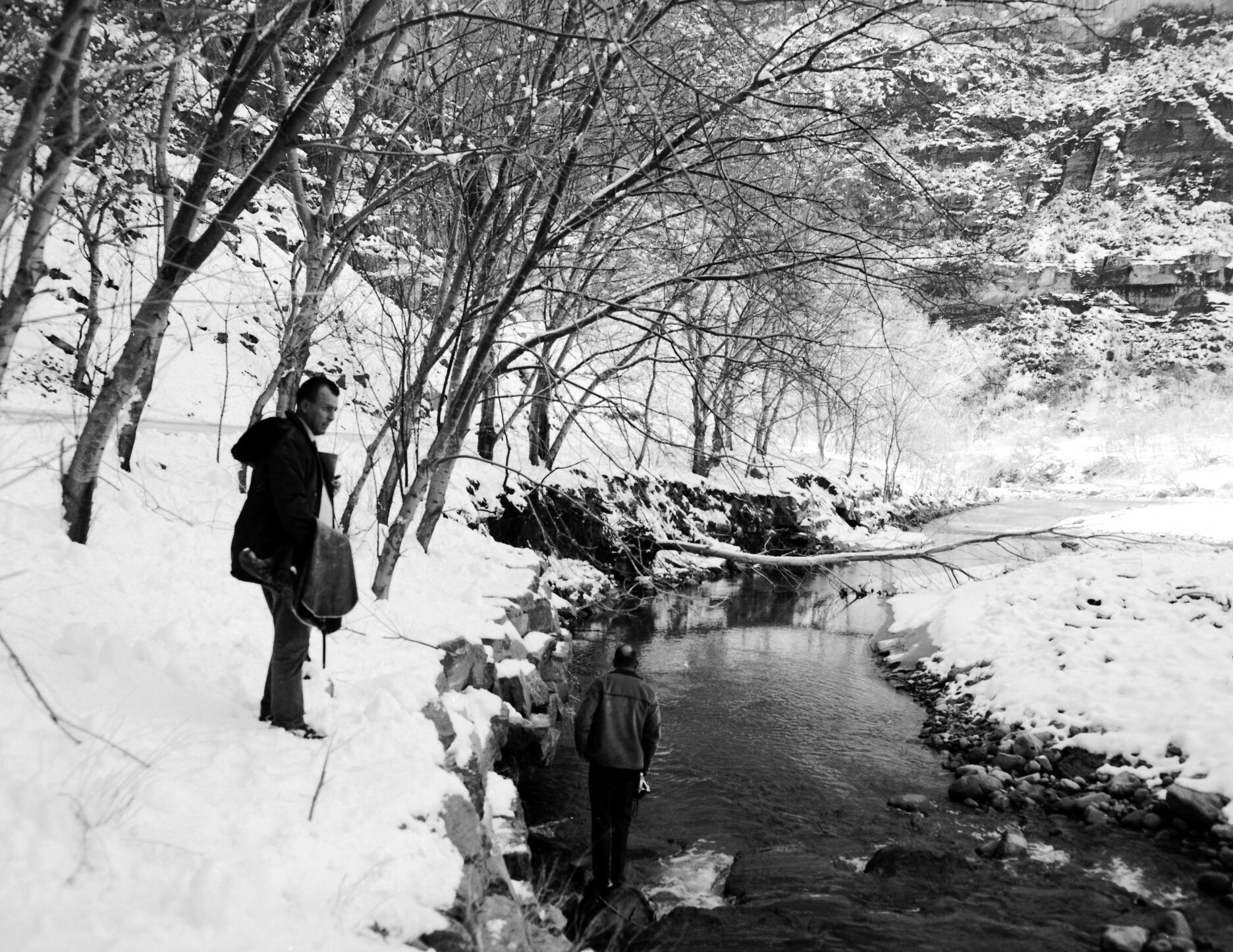 Flood damage to Virgin River bank. Image shows two men standing on riverbank in snow.