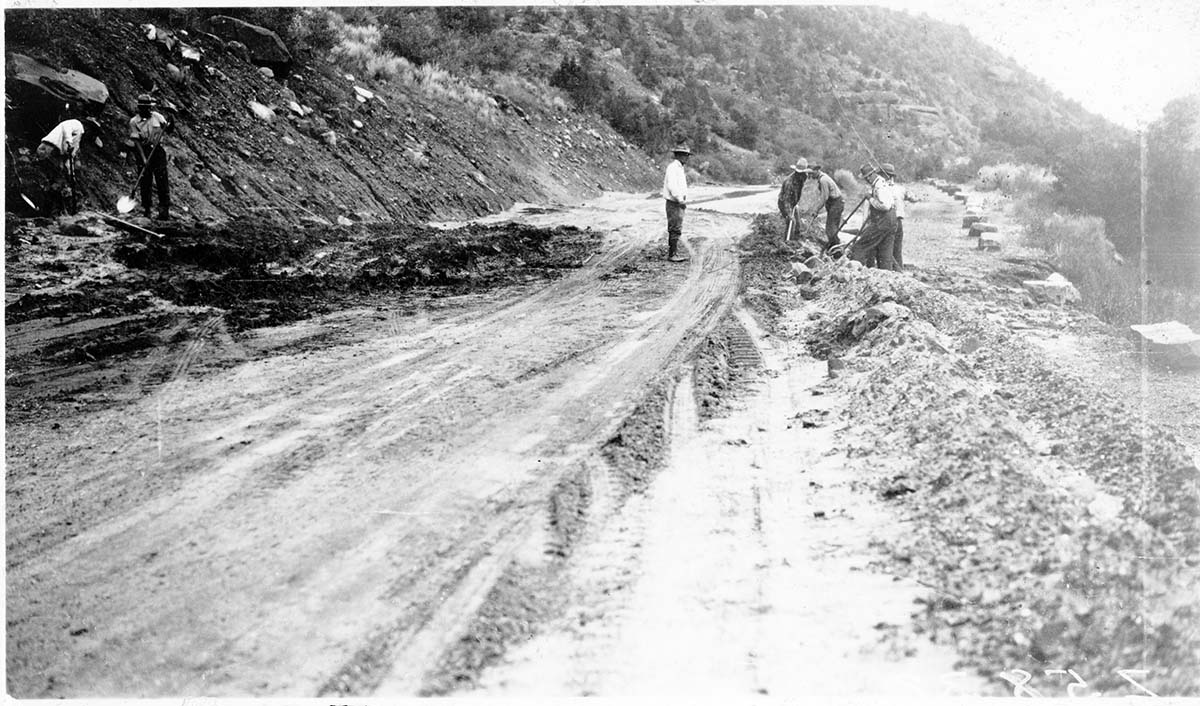 Storm damage, mud and debris on highway. Workers clearing street.