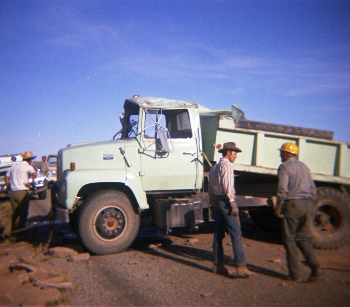 Color Photo of a damaged dump truck- tailgate and side ripped open.