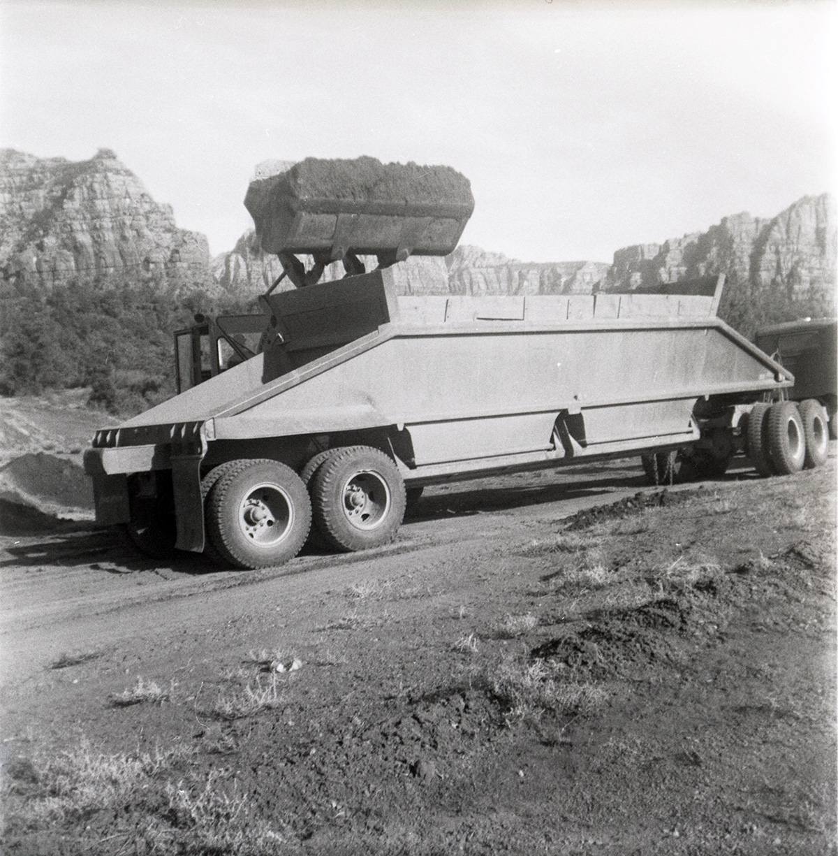 Excavator dumping pile of dirt into back of construction truck during road grading to Chamberlain Ranch and the Narrows.