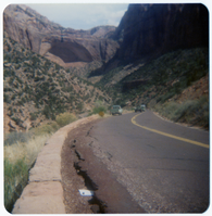 Crack in road in need of repair with paper marking over top, with Zion landscape in background.