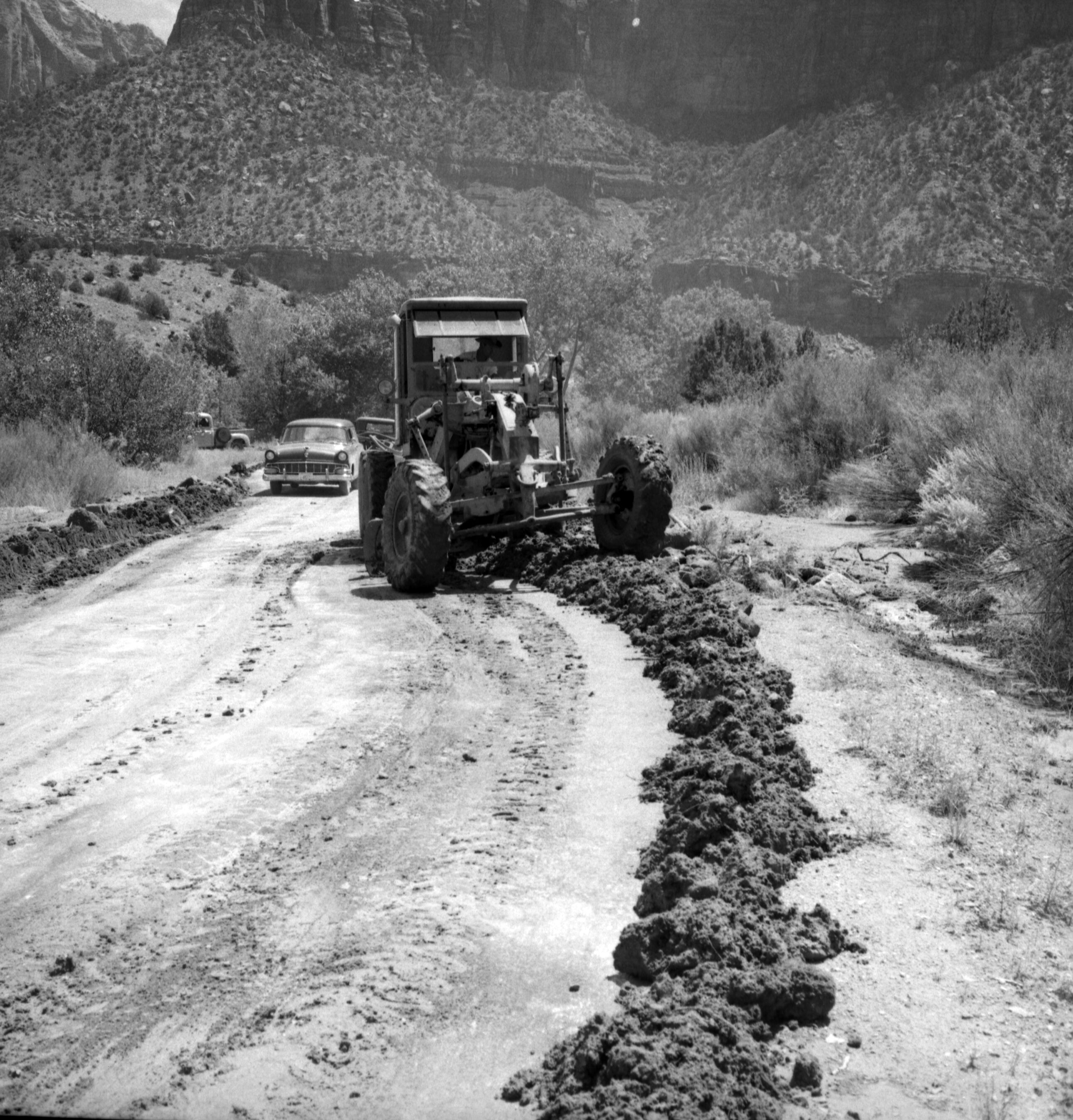 Grader clearing debris from roadway after flood damage.