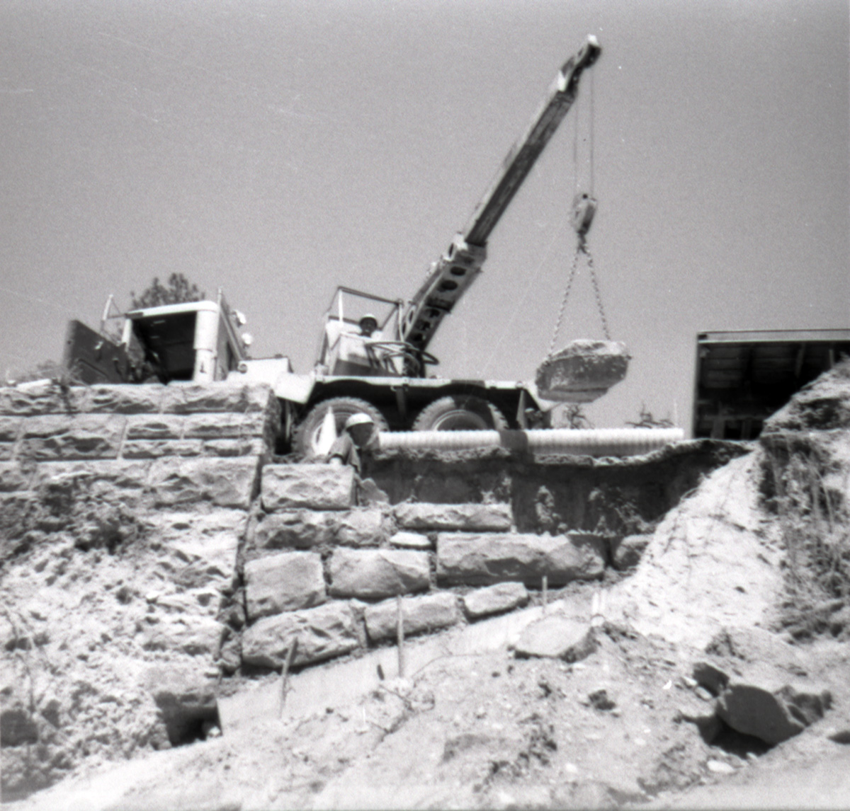 Man operating a crane lifting a rock during the retaining wall repairs along the East Rim road.