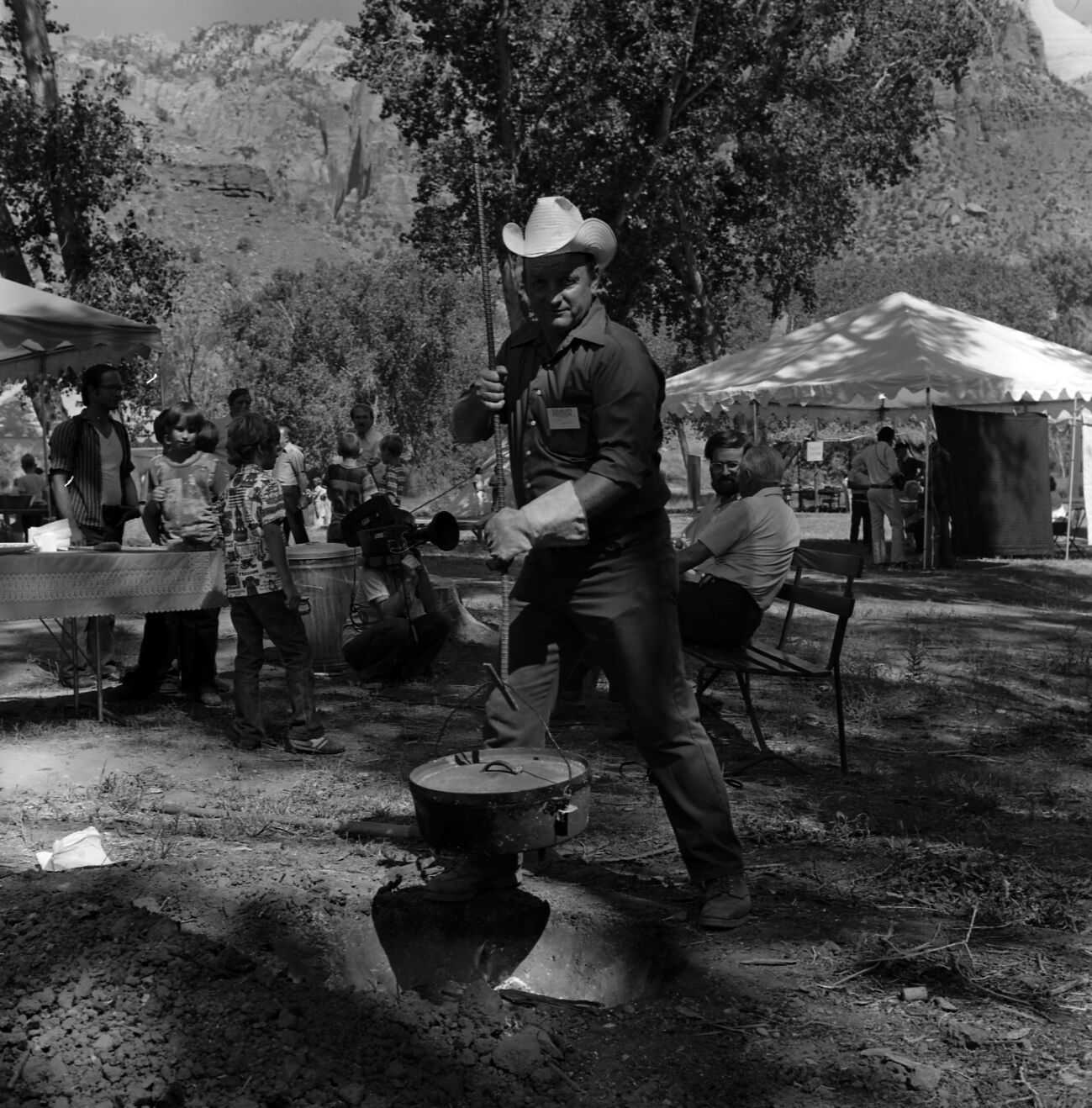 Doyle Winder lowers Dutch oven into fire pit during cooking demonstration at the second annual Folklife Festival, Zion National Park Nature Center, September 1978.