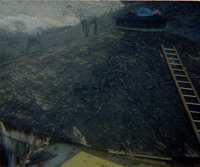Two men removing shingles from water tank during reroofing project.