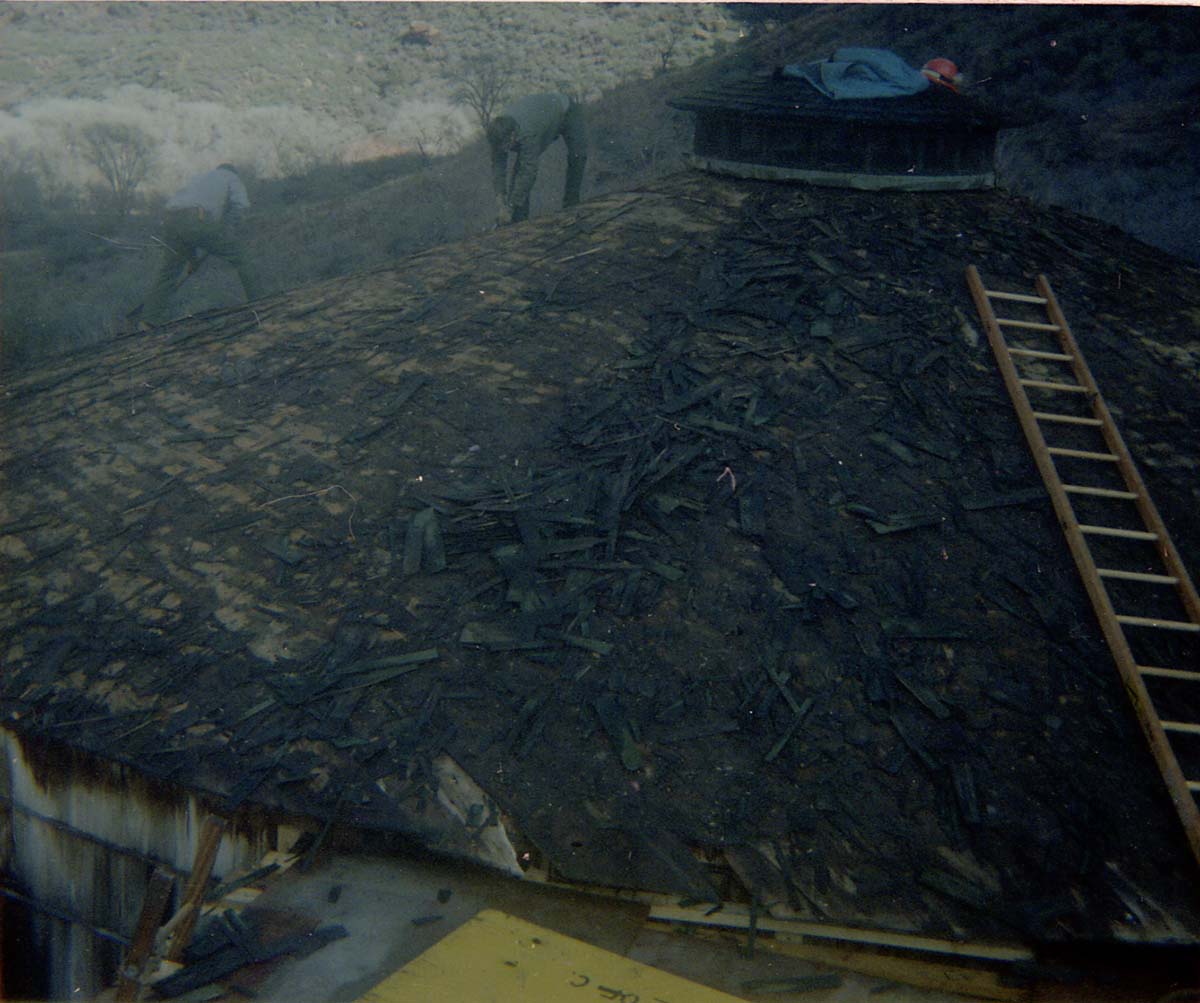 Two men removing shingles from water tank during reroofing project.