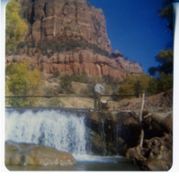 Man standing next to the Birch Creek Dam, suspension footbridge in background.