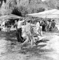 Springdale elementary school children perform a square dance under the direction of Principal Leon Lewis at third Folklife Festival at Zion National Park Nature Center. Jim Fraley, Joe Serna, Jim Felton (with pith helmet) and visitors in background. [No photo or positive. Fingerprints on the negative.]