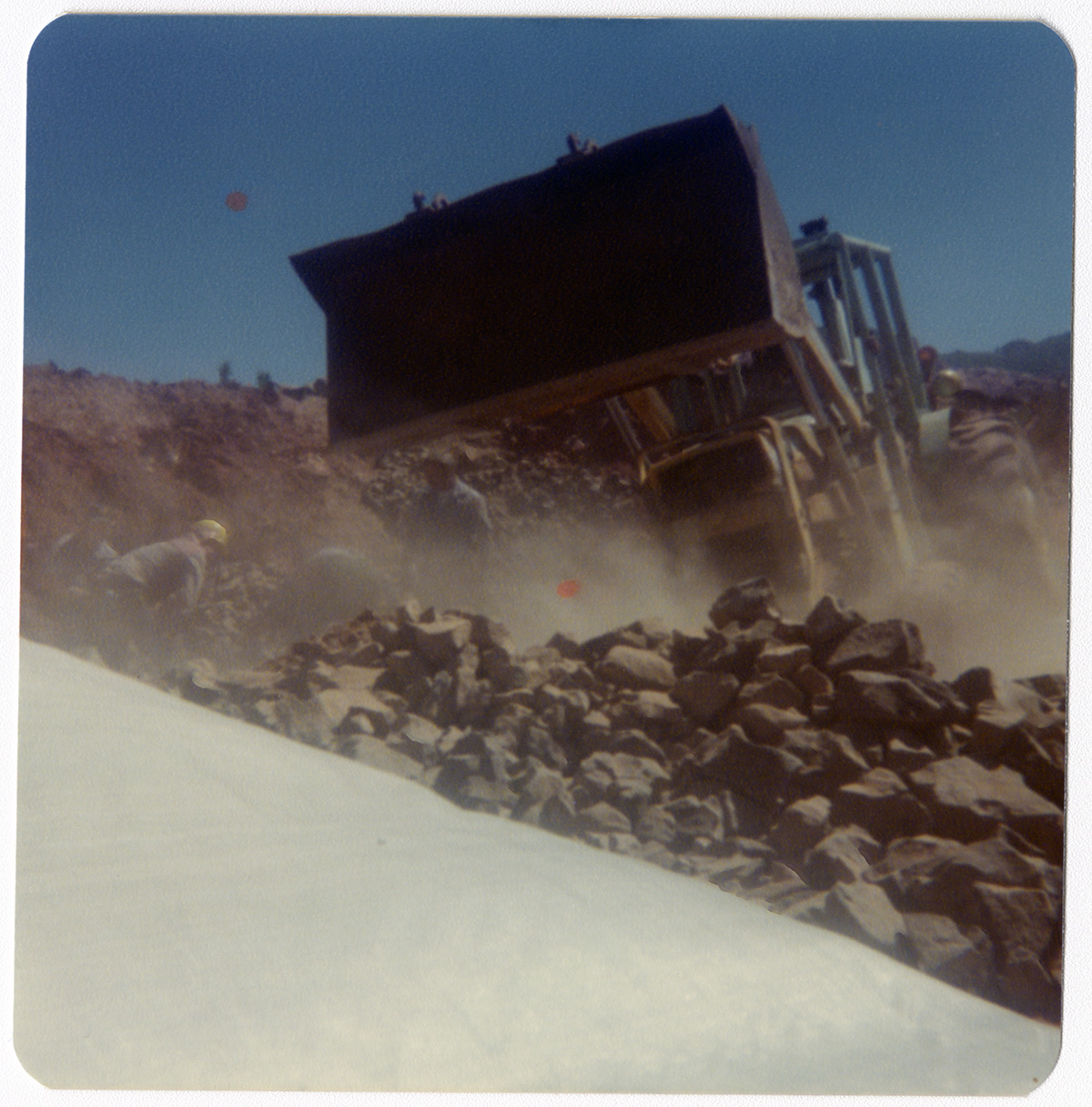 Excavator dumping rocks onto existing pile during road work/repair in Kolob Canyon.