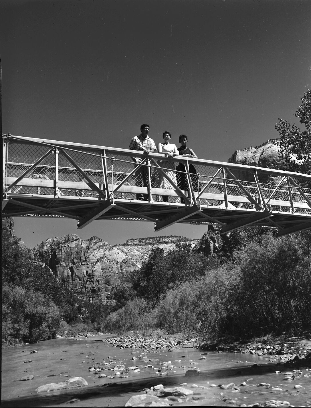 N. Akita, C. Smith and M. Groome pose on footbridge across Virgin River with Angels Landing and East Rim in background.