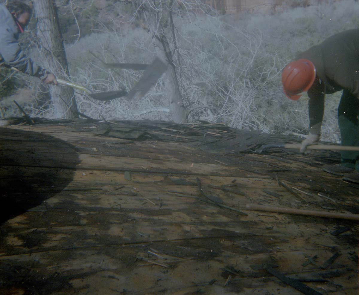 Two men removing shingles from water tank during reroofing project.