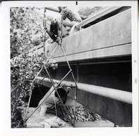 Workers place pipe on side of bridge during the Watchman housing utility project.