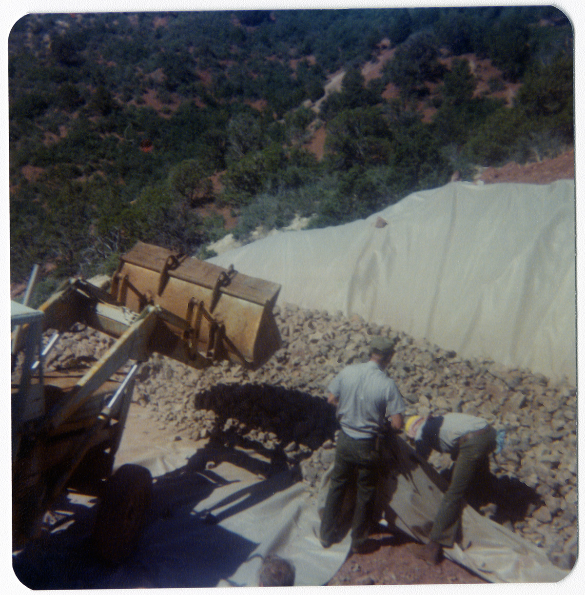 Rocks being place on tarp and men working on repairing road in Kolob Canyon.