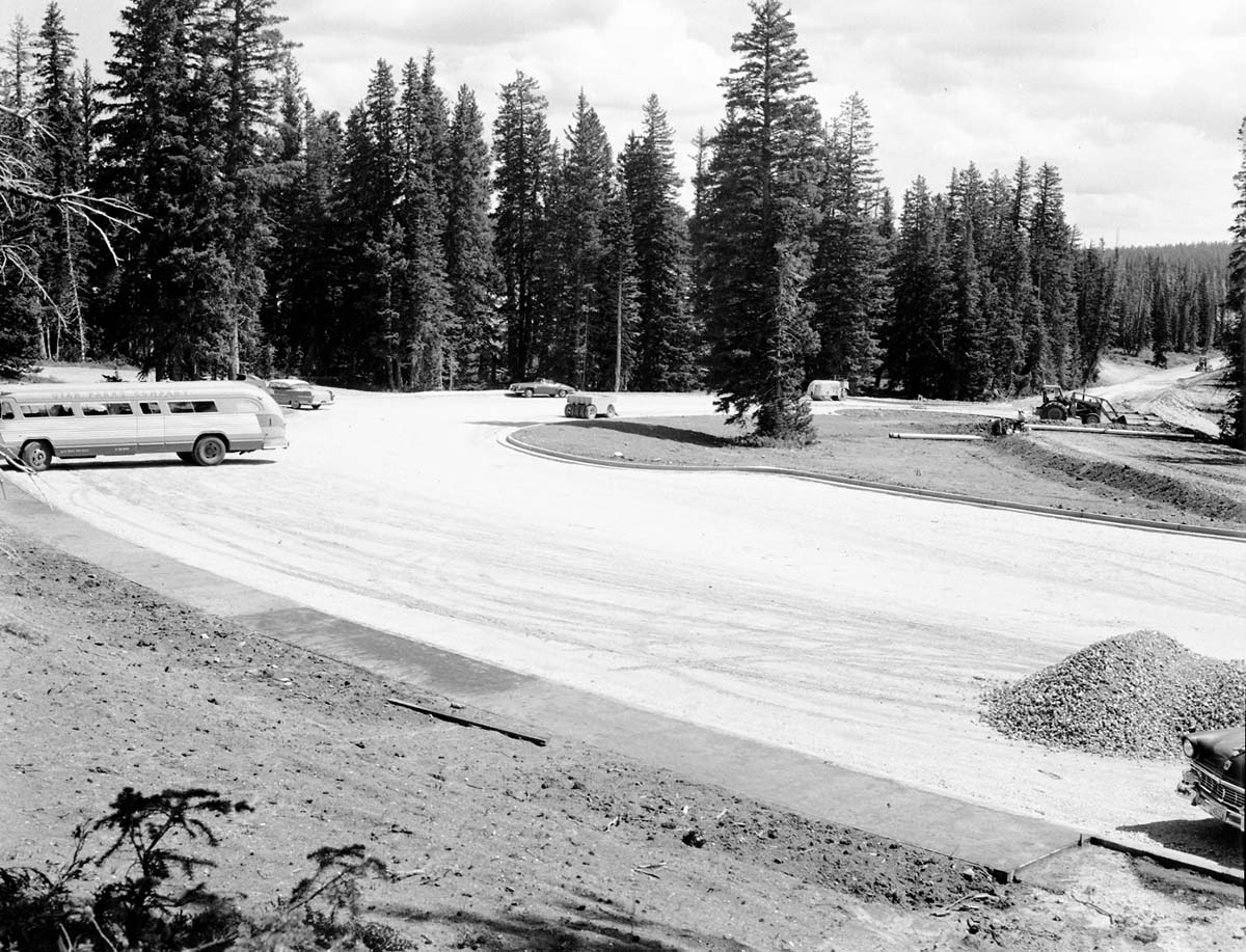 Cars in the partially constructed parking area at Point Supreme. Utah Parks Company bus parked at left, construction equipment at right. View back towards museum.
