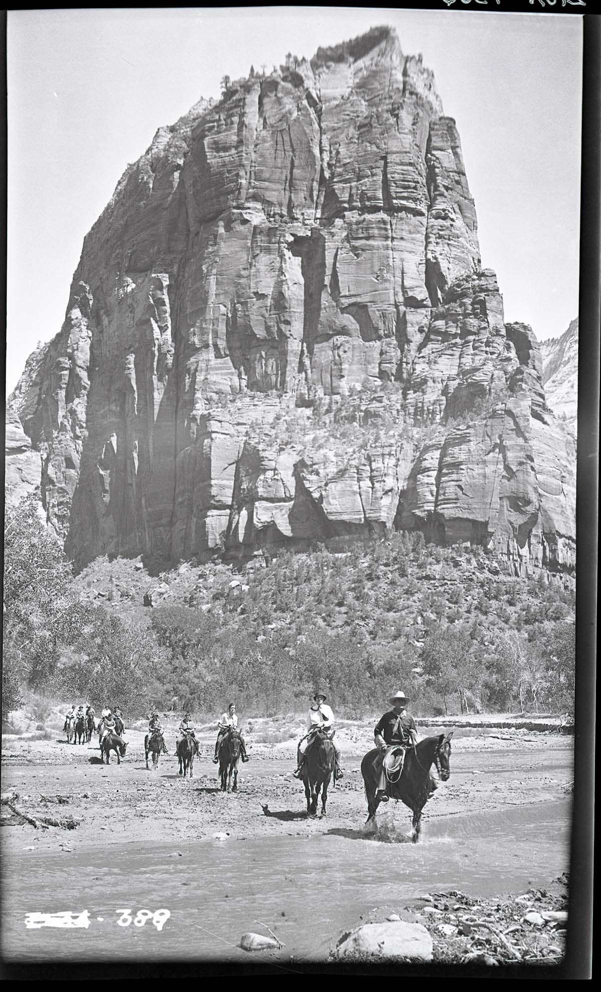 Horseback party crossing Virgin River, Angels Landing in background.