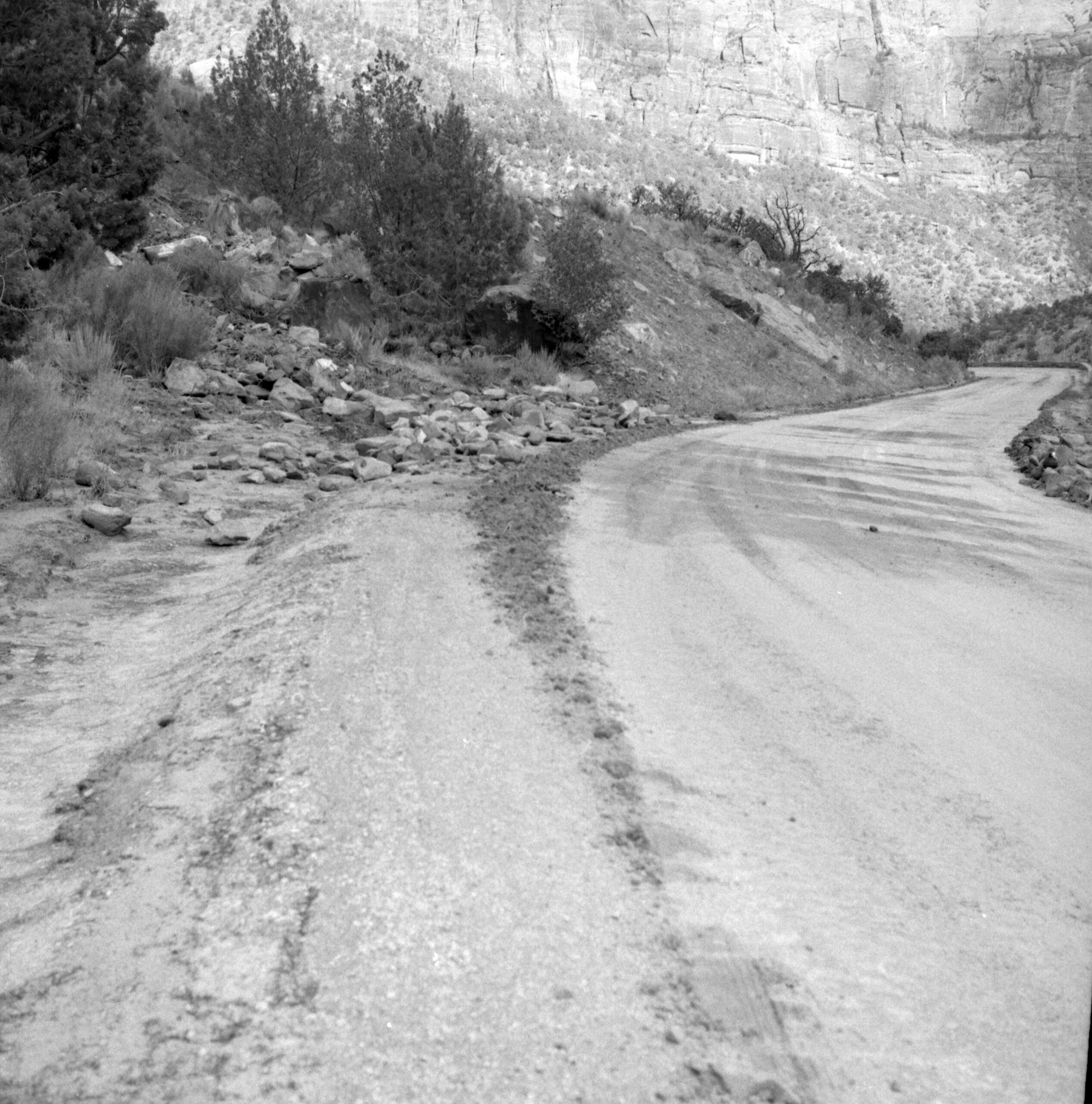 B&W negative of rock slide. Removing rocks from road with tractor- bystanders watching. [scratches, pits]
