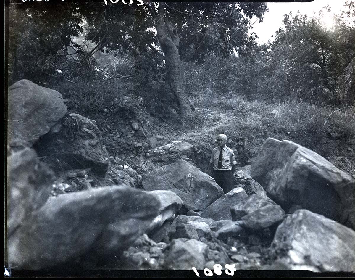 Damage done by storm of July 25, 1954 to West Rim Trail. Trail washout about a quarter mile from suspension bridge, Superintendent Paul R. Franke standing in wash.