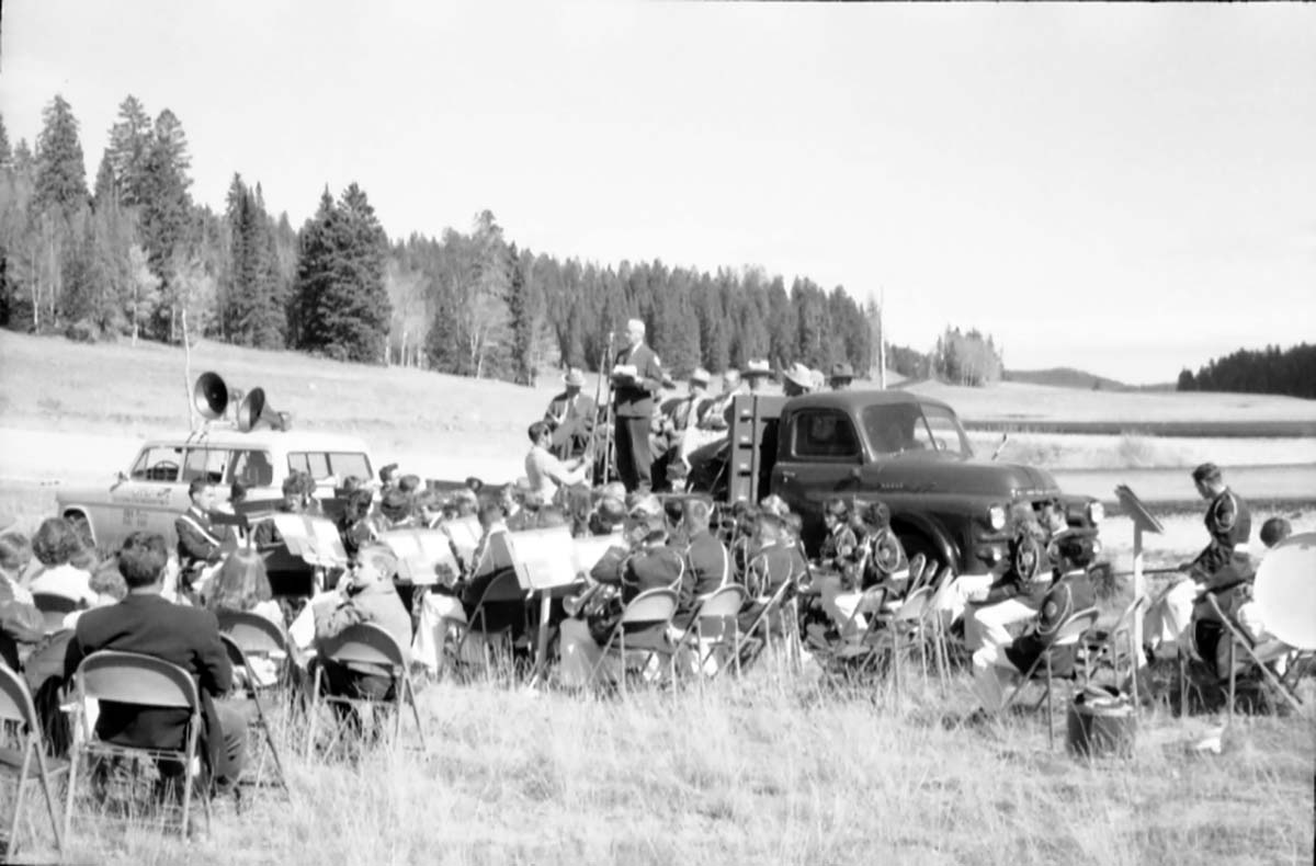 Dedication of Utah State Route 14 approach road. Master of Ceremonies Paul Franke, Zion and Bryce Canyon Superintendent, stands on truck bed and introduces speakers to onlookers in a meadow. Band seated at right.