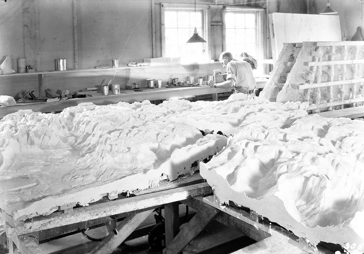 View of interior of Civil Works Administration (CWA) College Avenue laboratory showing plaster cast of Zion relief map. Background: interior of shop facility and worker.