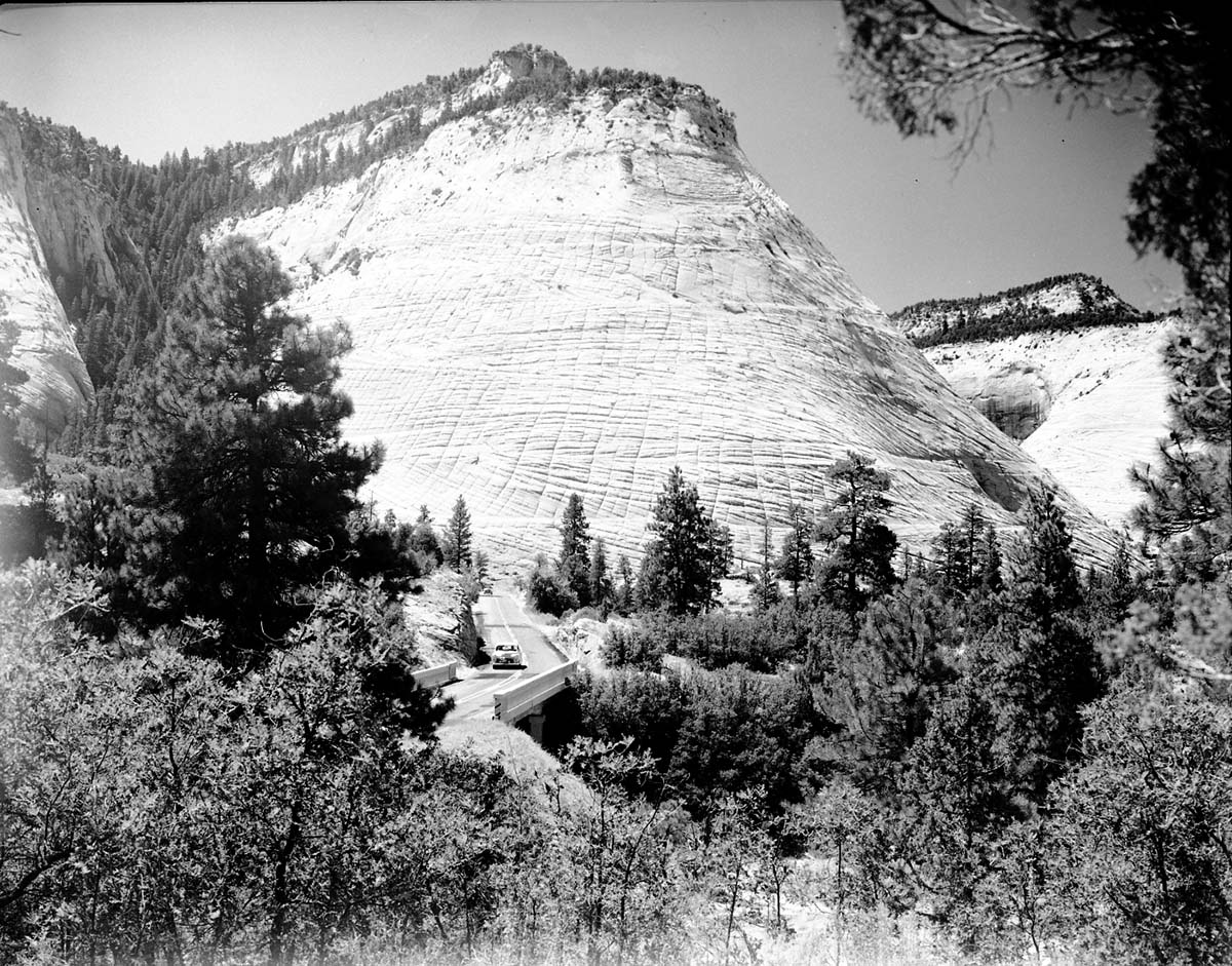 Cars driving on the Zion-Mt. Carmel Highway at the foot of Checkerboard Mesa.