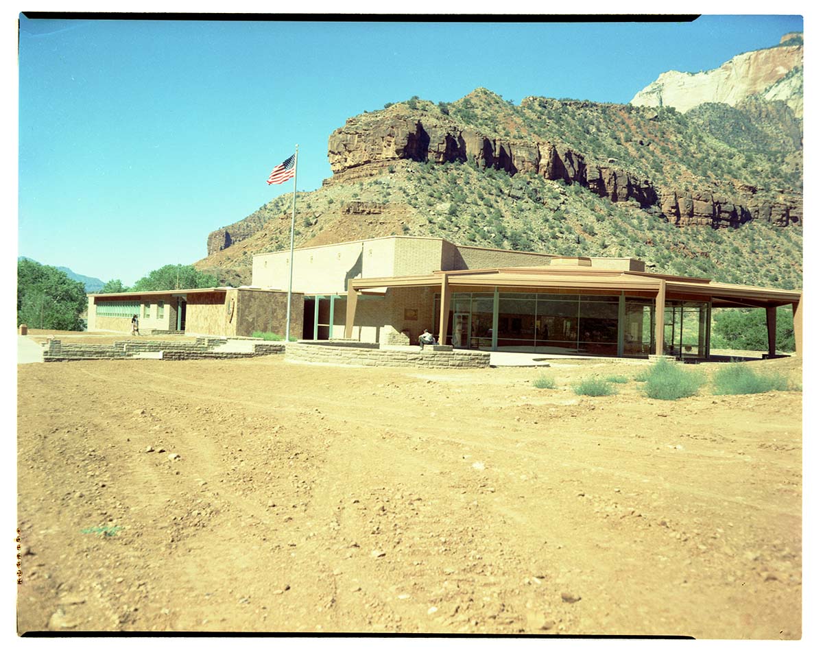 Exterior of old Mission 66 Visitor Center and Museum, with dirt lot surrounding building.