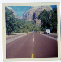 Two-way road divided by yellow dotted lines with Zion landscape in background.