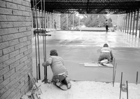 Workers leveling cement in corner during construction of headquarters addition.