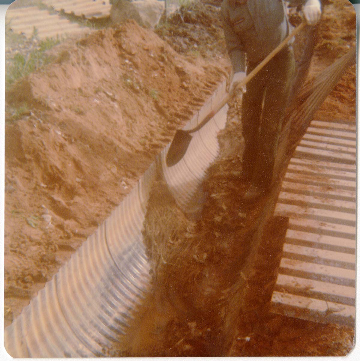 Man shoveling away dirt to uncover the irrigation ditch in South Campground.