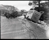 Accident involving a Wonder Bread truck which slid off road east of small tunnel because of icy road and too much speed, saved by large pine tree. Wrecker and several people assisting.