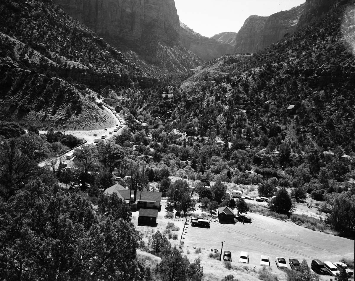 Oak Creek bridge and view of canyon- group of 75 motorhomes in caravan called the Fireballers, preparing to drive through tunnel. Park administration buildings in foreground.