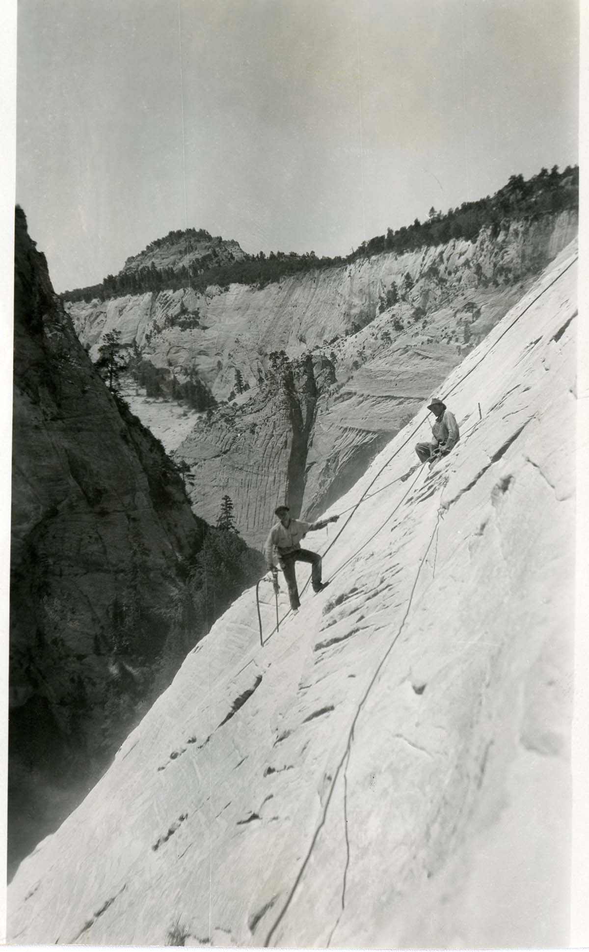 Two workers cutting the stone face for the West Rim Trail construction-1924.