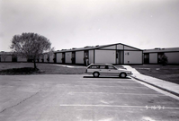 Barracks and parking area with man walking on sidewalk. Building number 5. [Image possibly for comparative housing study]