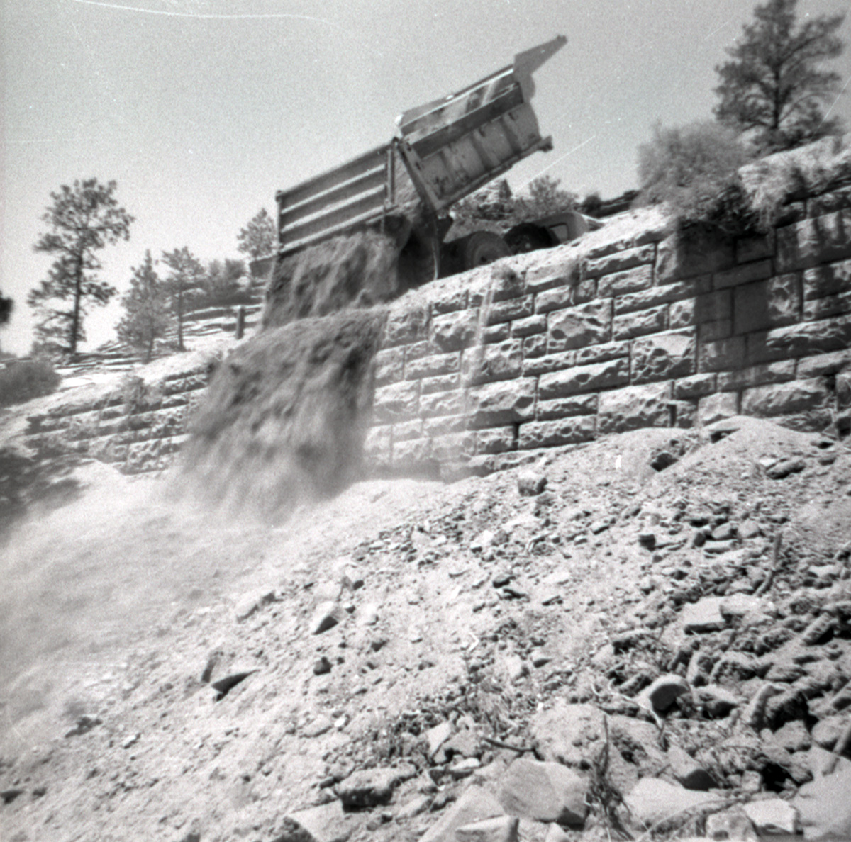 Dump truck dumping dirt over retaining wall during repairs of all along East Rim road.
