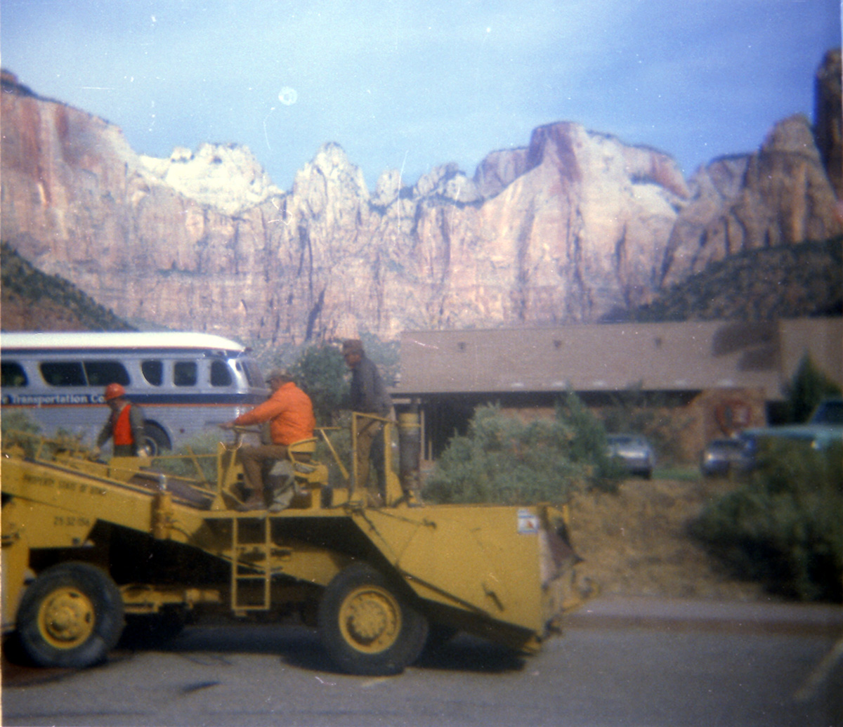 Men operating construction vehicle with building in background during sealcoating of parking are in Zion.