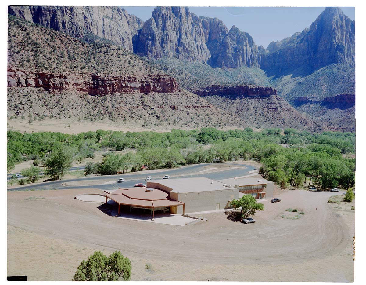 The old visitor's center and headquarters building and surrounding dirt lot, view south.