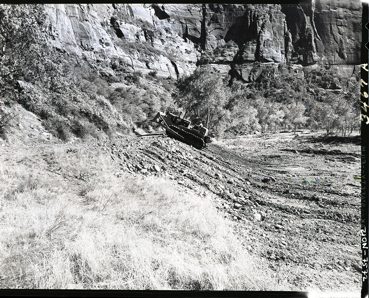 Road repair of flood damage on valley road by packing road slope with bulldozer.