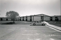 Barracks and parking area with man walking on sidewalk. Building number 5. [Image possibly for comparative housing study]