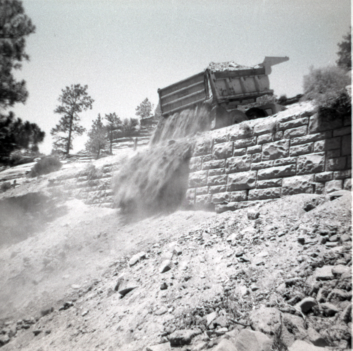 Dump truck dumping dirt over retaining wall during repairs of all along East Rim road.