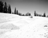 Rock aggregate piles on rim road, prior to graveling road. Man standing next to pickup truck.