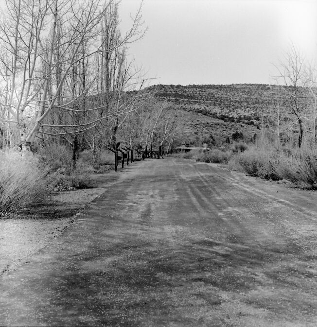 Wayside panel exhibit and plow next to the road and footbridge leading to residential area.