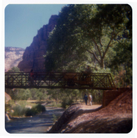Man driving sweeper equipment across the new Grotto footbridge after its placement on stone abutments. Men working on trail in background.