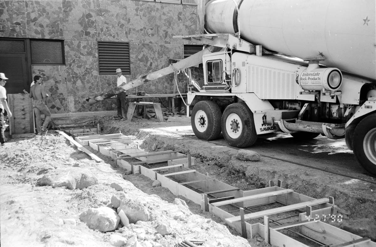 Workers operating a cement construction vehicle during construction of headquarters addition.