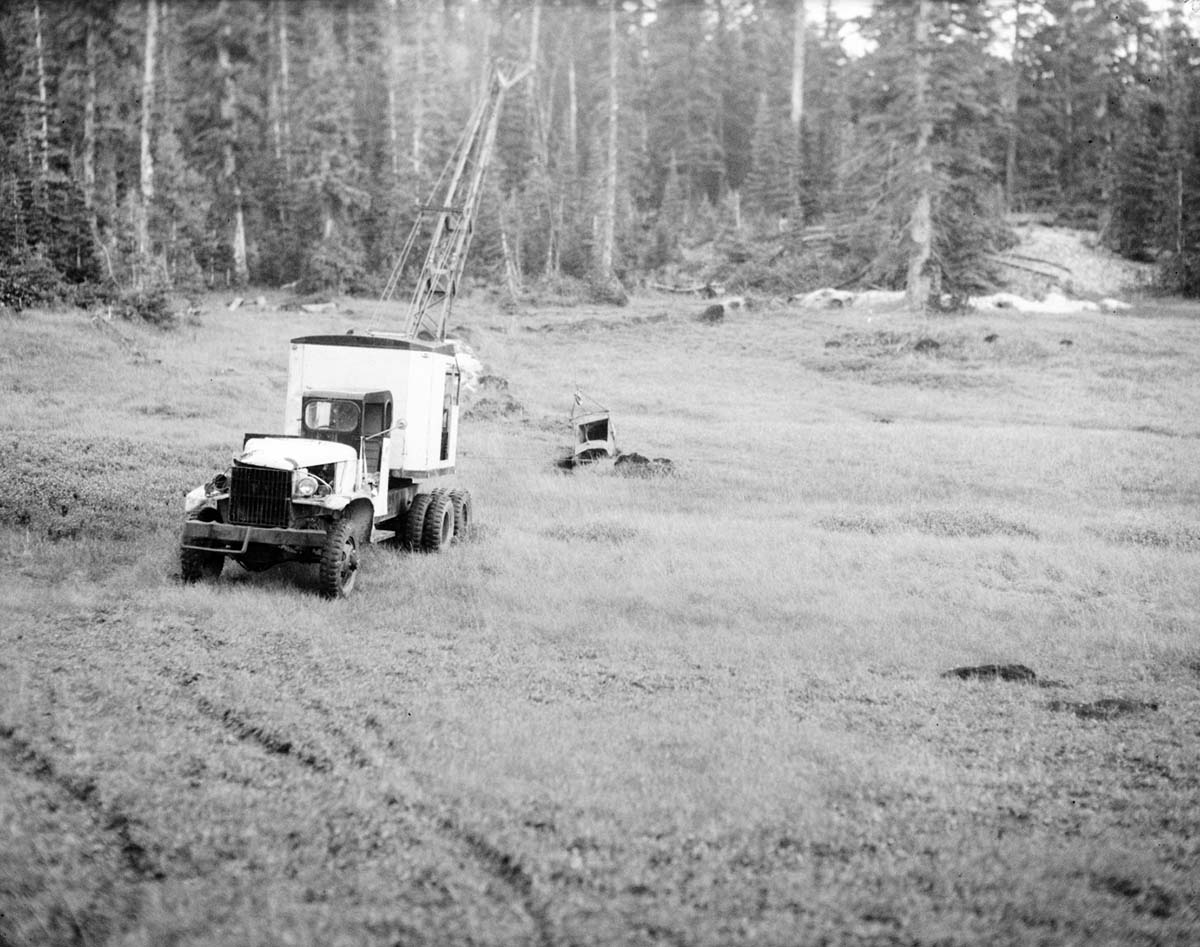 Truck, crane, and digging equipment in meadow for water exploration.
