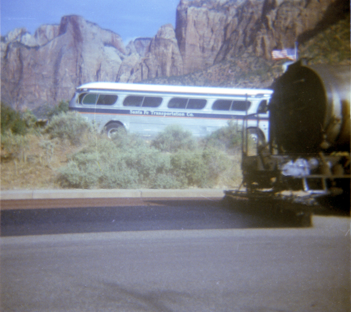 Construction vehicle sealcoating parking area in Zion with bus in the background.