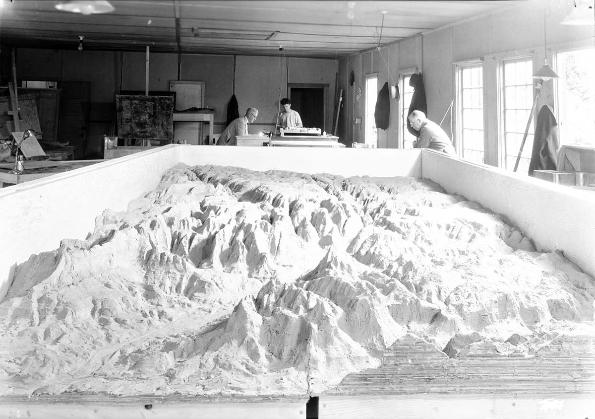 Clay model of Zion National Park relief model map. Civil Works Administration (CWA) College Avenue laboratory. Three men working in the background.