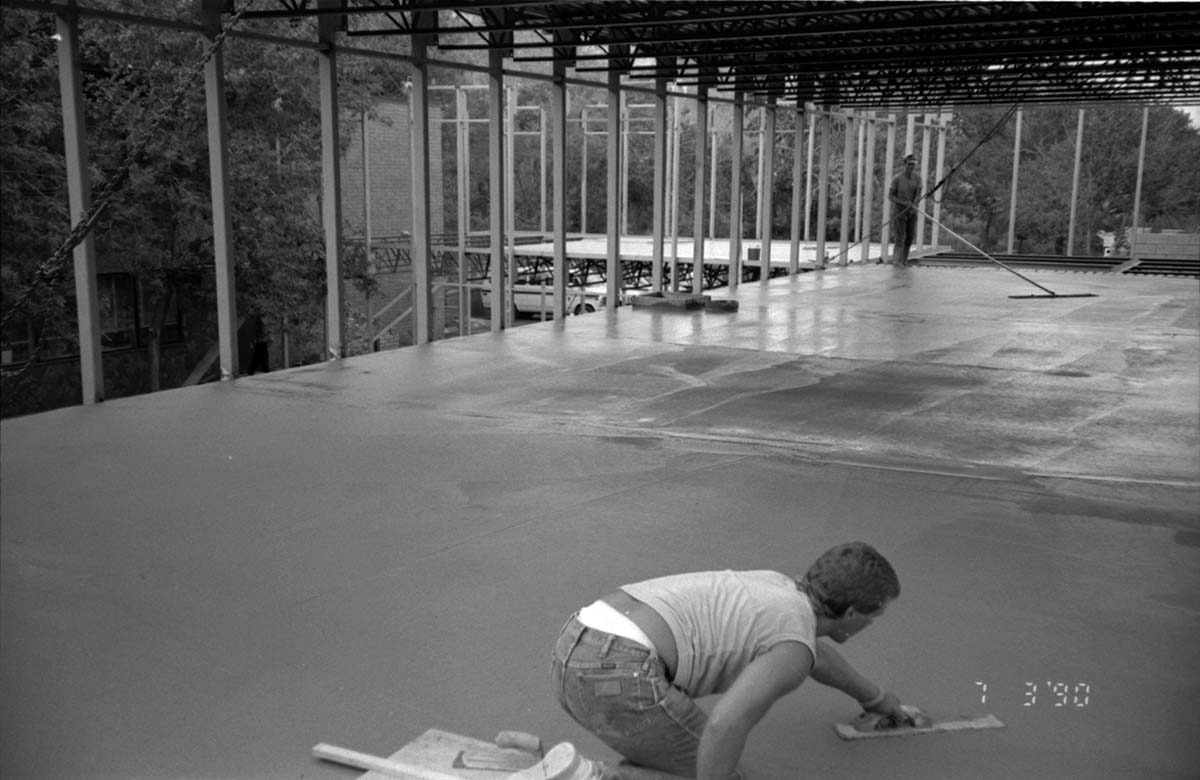Man leveling cement in corner during construction of headquarters addition.