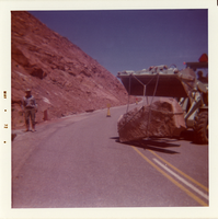 Construction vehicle transporting large boulder across road during road repair of Kolob Canyon Road.