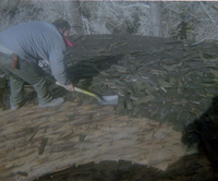 Man using shovel to clear old shingles from water tank during reroofing project.