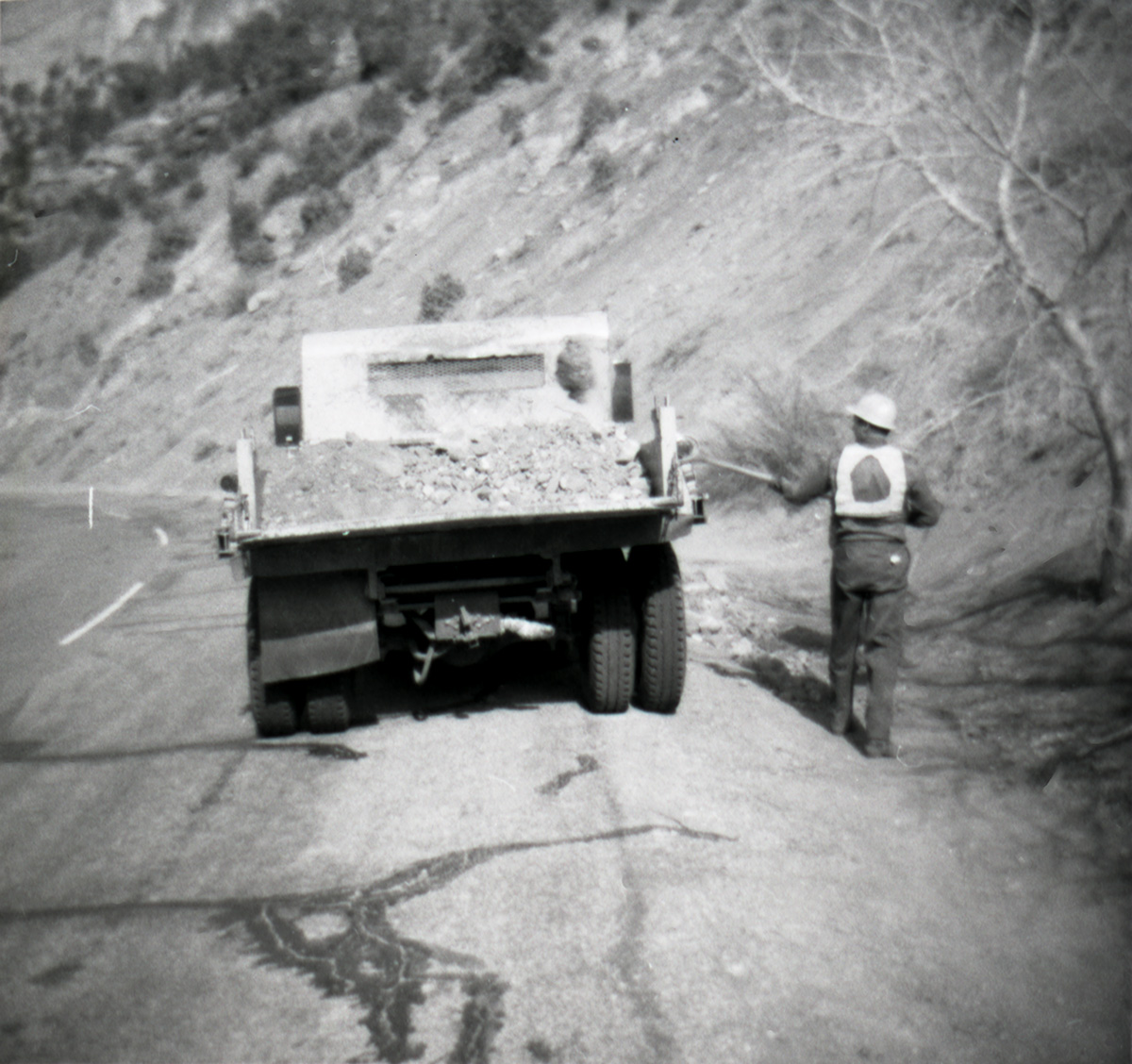 Man shoveling dirt from back of truck to use during road work.